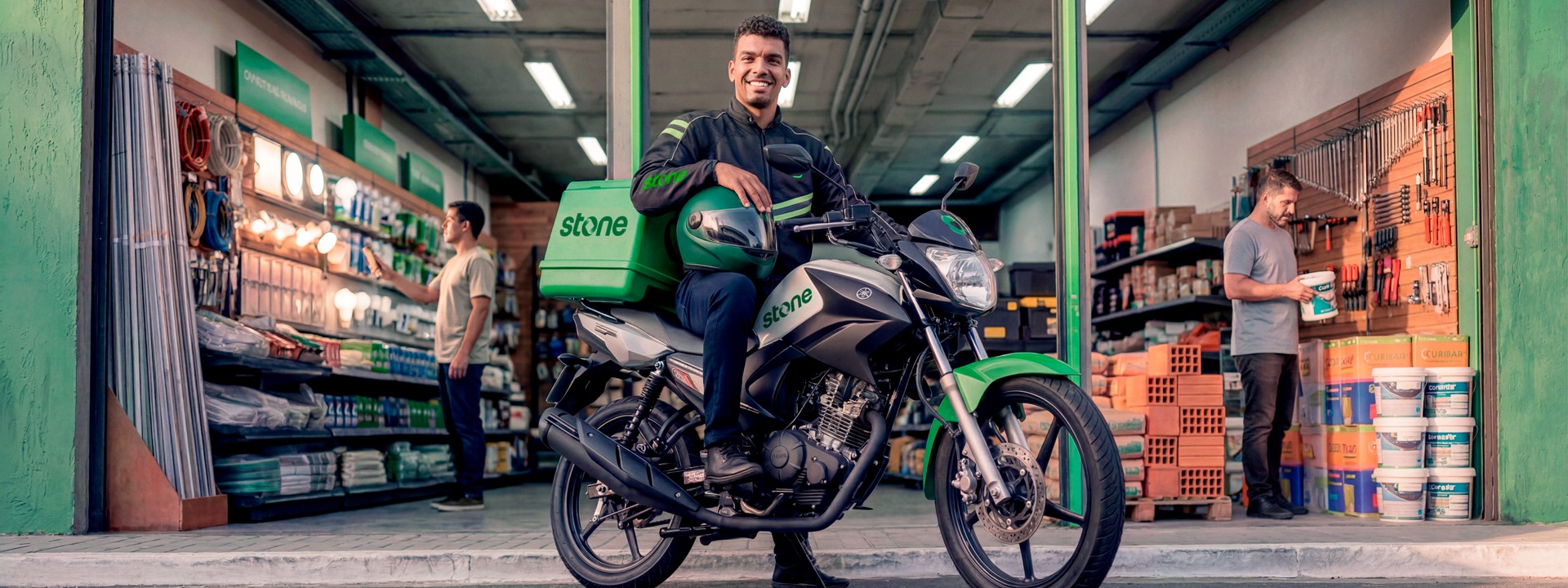 Polo Angel Stone com moto e baú da marca em frente a uma loja