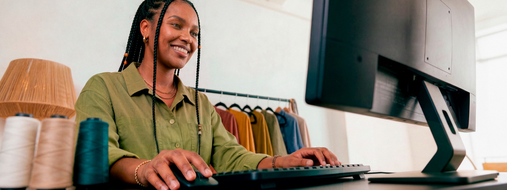 Empreendedora sorridente em ateliê de tricô digitando no teclado do computador