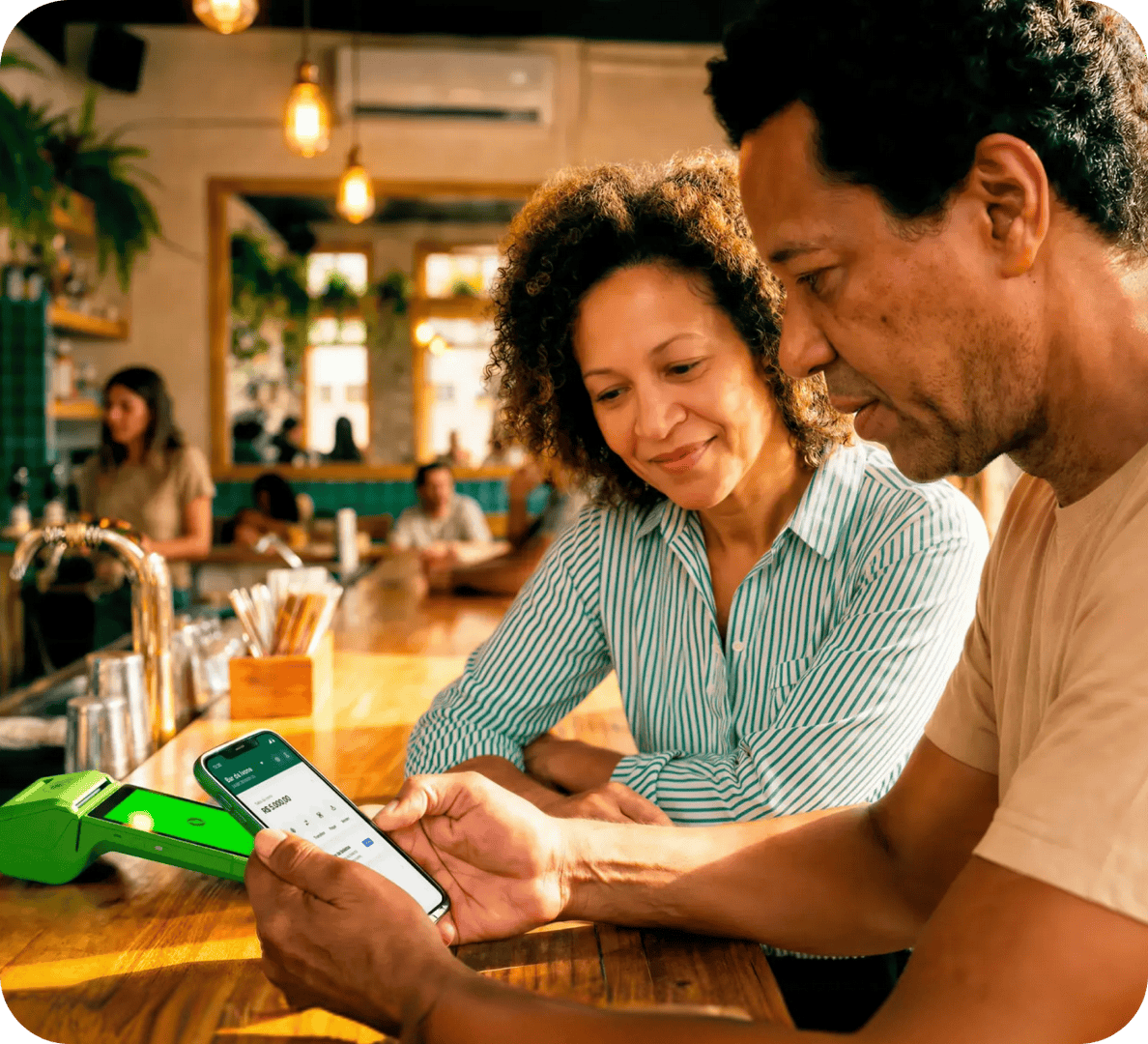 Empreendedores analisando o seu Capital de Giro no celular em seu estabelecimento e com a maquininha Stone ao lado