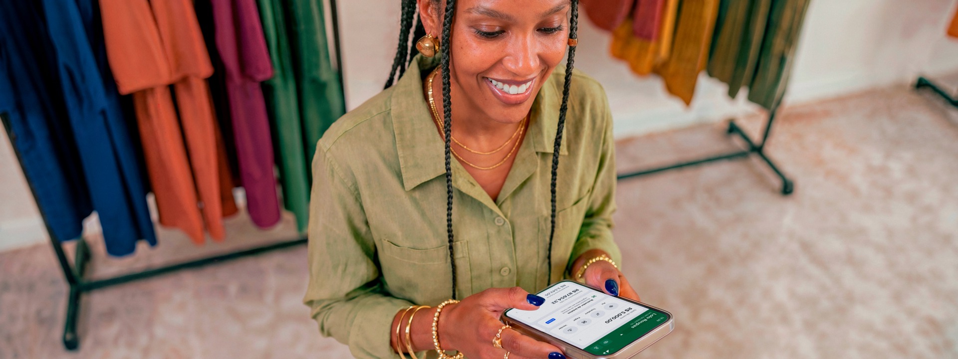 Empreendedora em loja de roupas sorrindo enquanto consulta o app Stone no celular