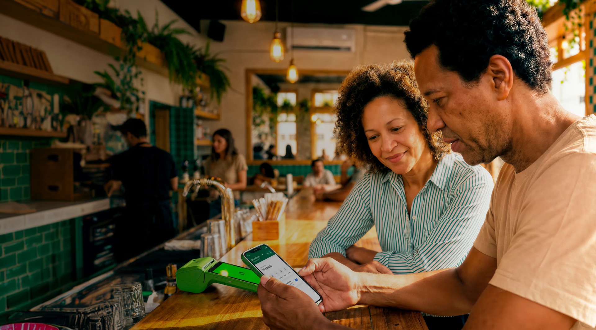 Empreendedores analisando o seu Capital de Giro no celular em seu estabelecimento e com a maquininha Stone ao lado