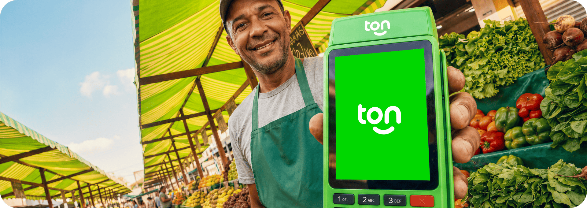 Empreendedor sorrindo segurando a maquininha Ton em sua banca de hortifruti