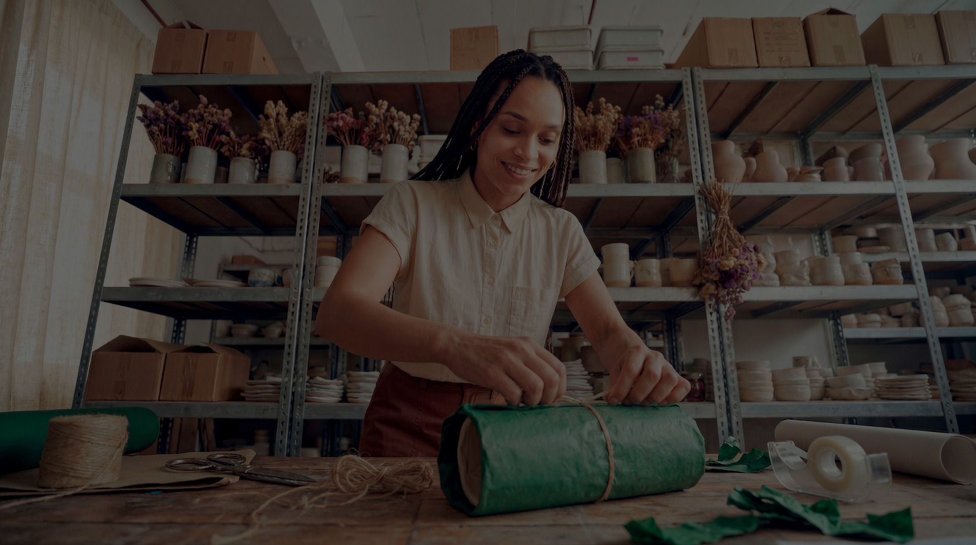 Empreendedora embalando produto com papel verde em ateliê de cerâmicas