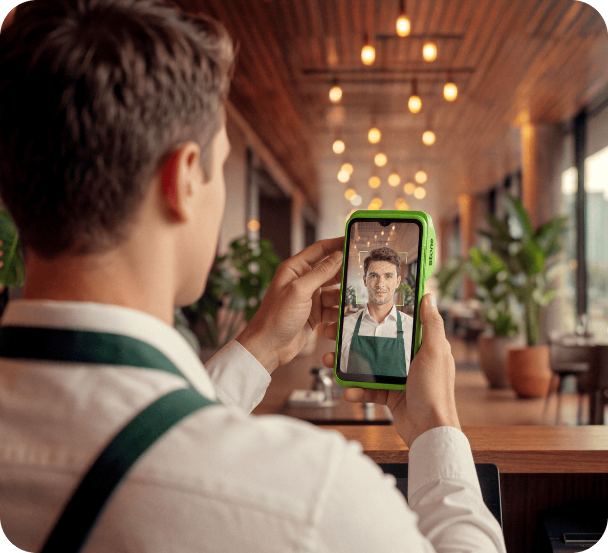 Garçom em restaurante usando o app Stone no celular para fazer uma chamada de vídeo com cliente