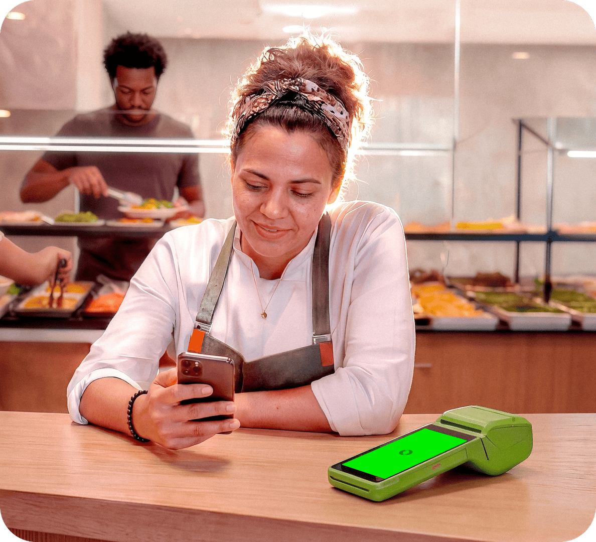 Empreendedora usando o celular ao lado da maquininha Stone em um restaurante