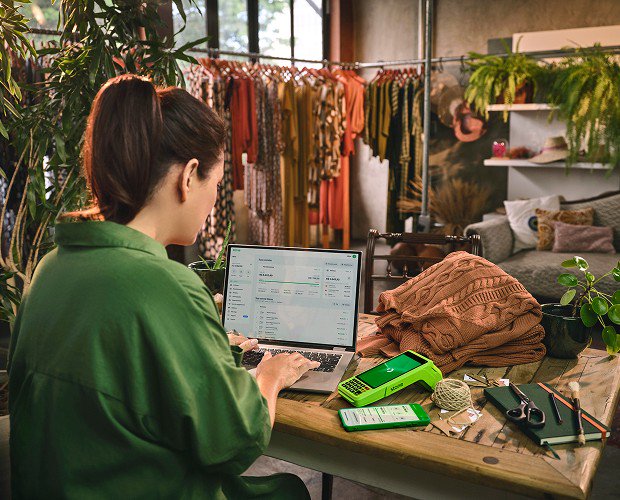 Mulher mexendo no computador ao lado da maquininha da Stone