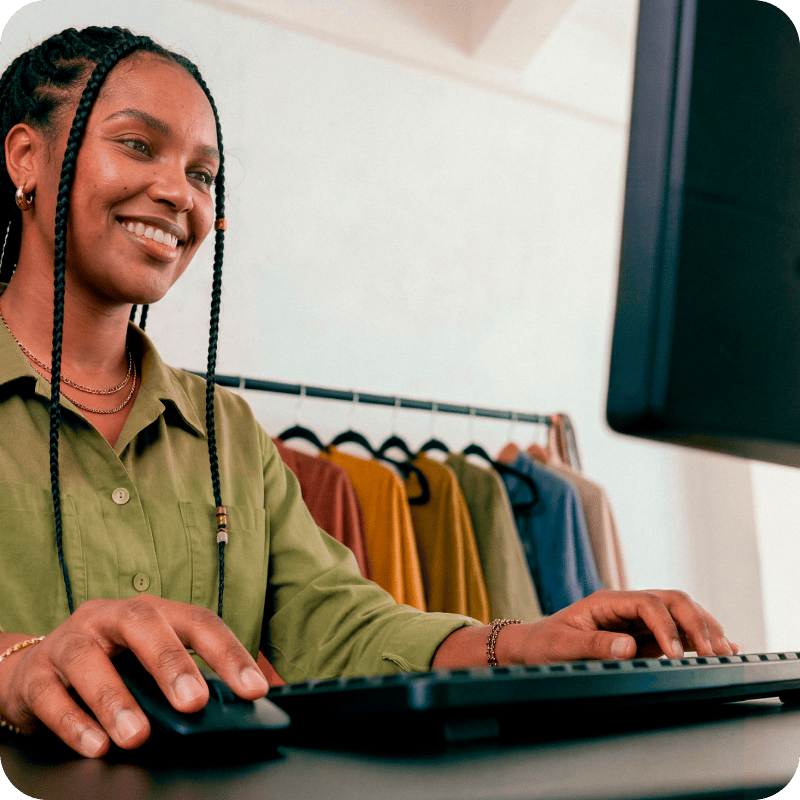 Empreendedora sorrindo enquanto trabalha no computador em sua loja de roupas