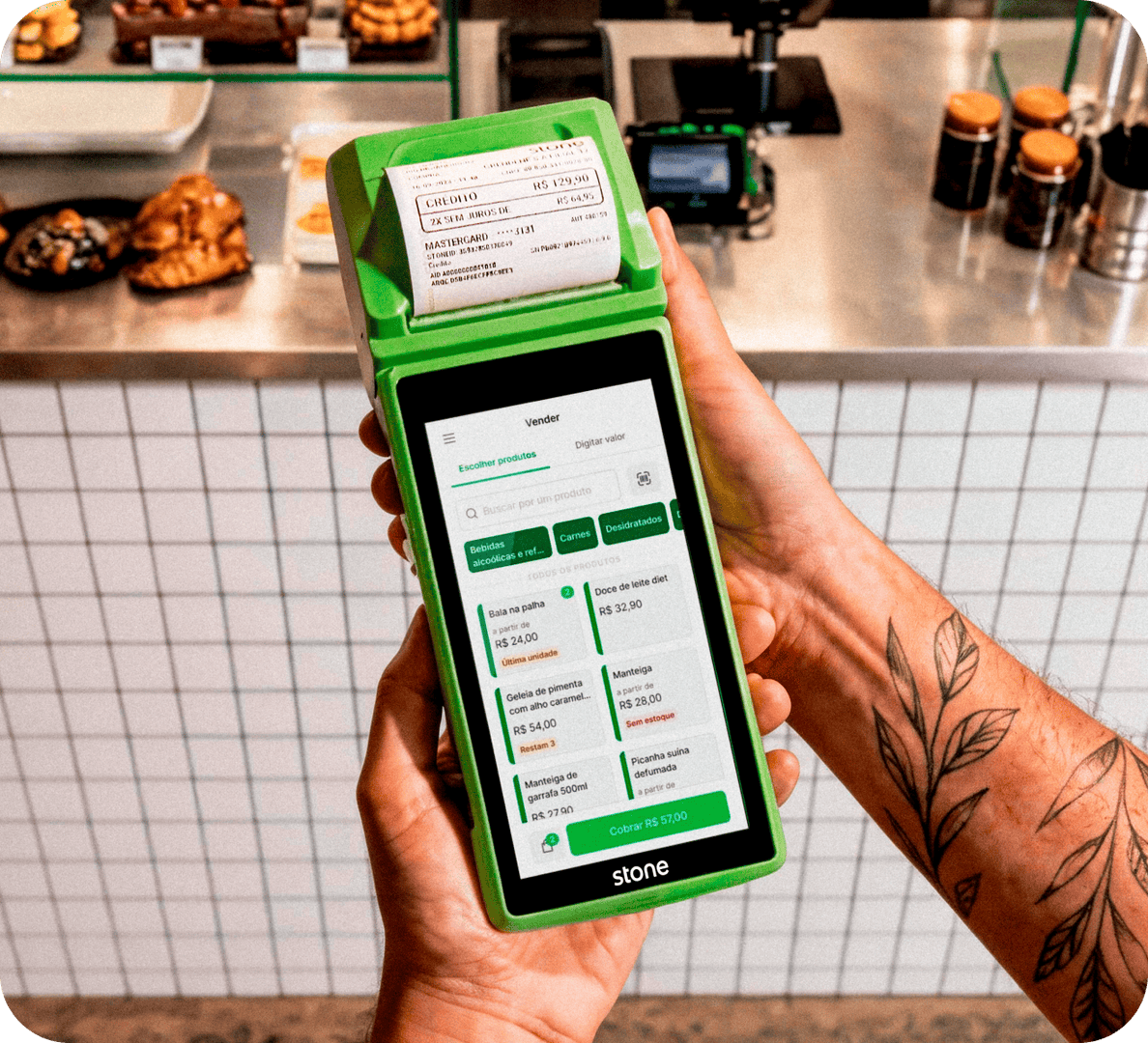 A empreendedora em sua loja de roupas, com linhas de costuras atrás está segurando um celular para enviar o link de pagamento aos seus clientes através do Messenger do Facebook, Whatsapp e Instagram.