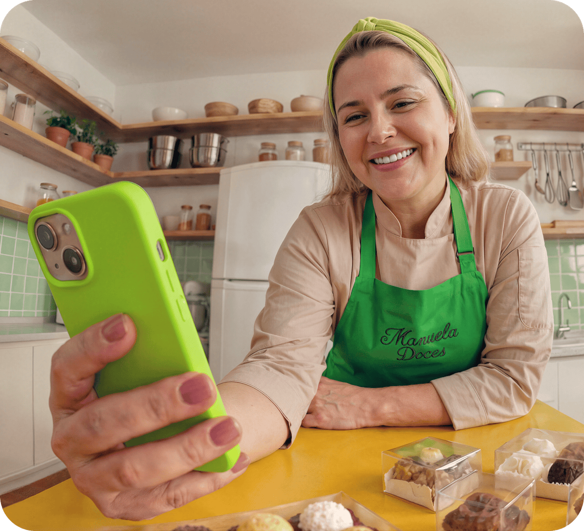 Empreendedora confeiteira sorrindo enquanto usa o celular em sua cozinha