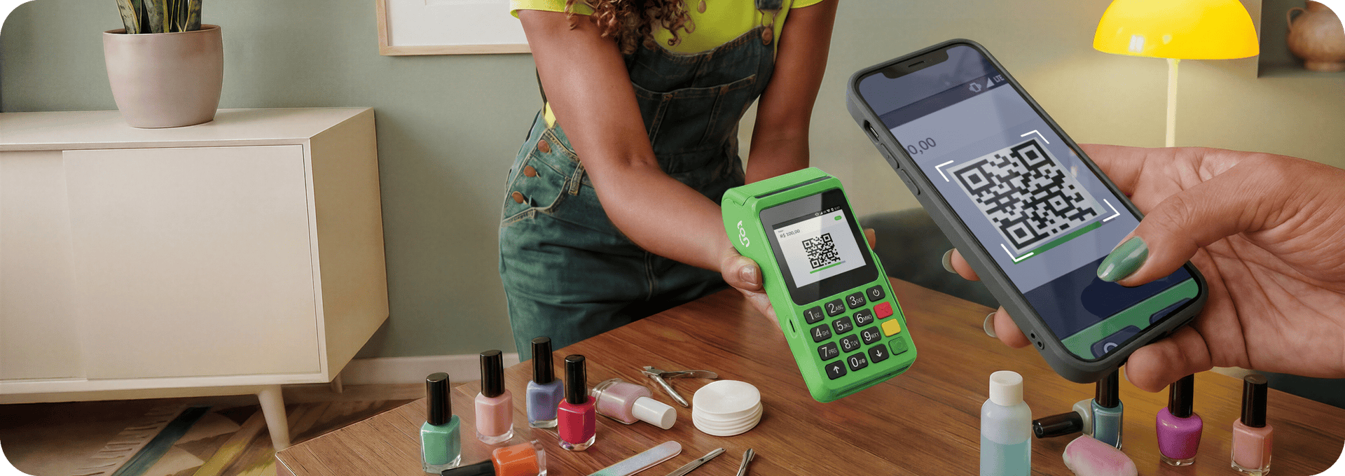 Empreendedor sorrindo, segurando a maquininha do Ton em sua mão esquerda, uma cliente está em sua frente também sorrindo e aproximando seu celular sobre a tela da maquininha para ler o QR Code que aparece na tela e realizar um pagamento via Pix.