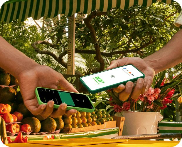 Empreendedora está utilizando o seu celular como Máquina de Cartão e o cliente está passando o seu cartão por aproximação. Ao lado estão alguns cupcakes e utensílios de cozinha. 