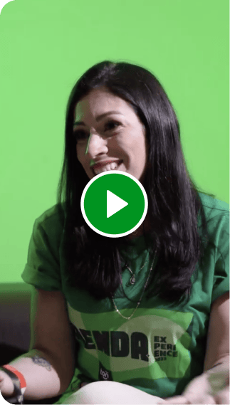 Consultora Renda Extra Ton. Mulher sorrindo, com camisa verde sentada em um sofá marrom, sorrindo, em um ambiente verde aconchegante.