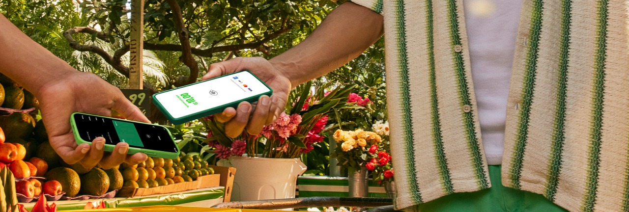 Empreendedor na sua barraca de laranja na feira com o seu celular recebendo o pagamento pelo Tapton, a maquininha no celular por aproximação do seu cliente.